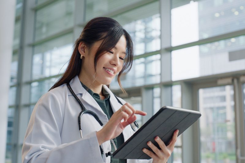 Asian woman, doctor and happy in hospital with tablet for public service, results and committed. Female person, closeup and smile for healthcare with appointment, work and wellness in medical career